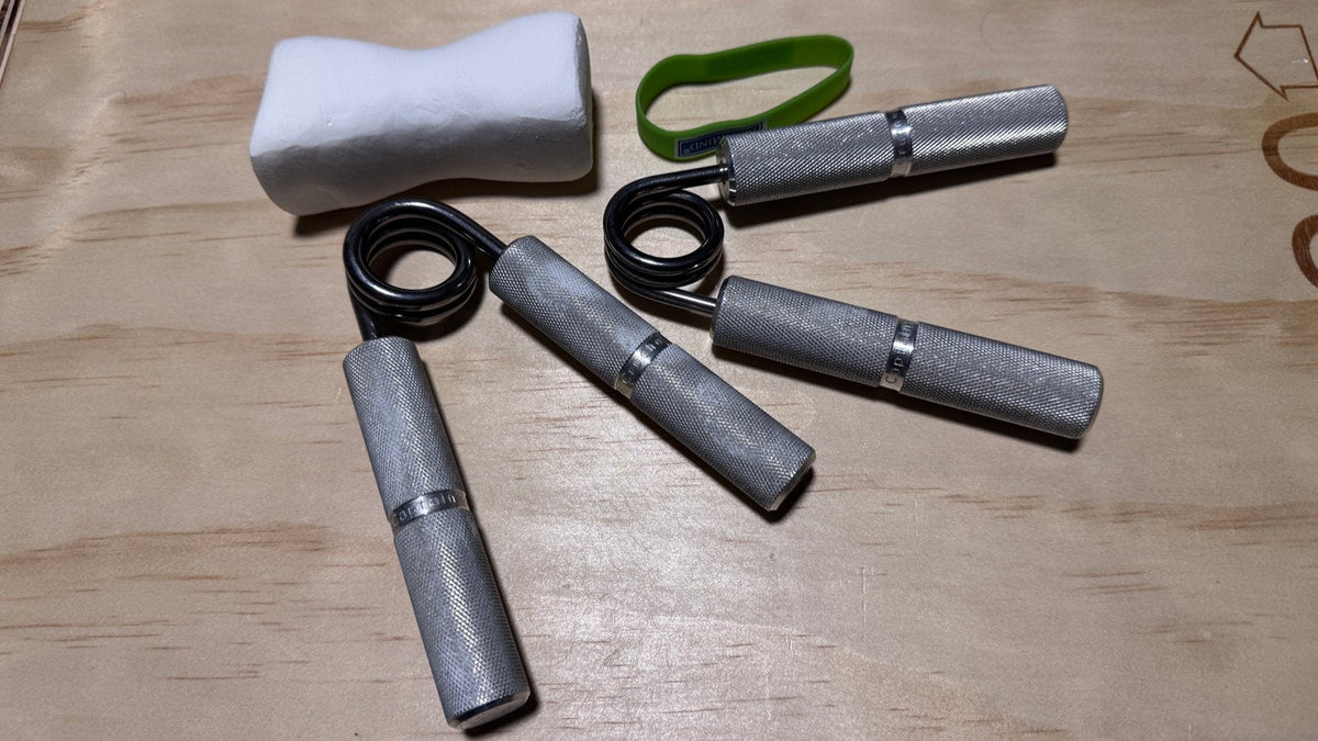 Beginner grip training kit: two hand grippers, an extensor band, and chalk laid out on a gym floor.